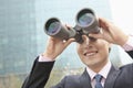 Smiling businessman looking through binoculars, blue reflection in the glass Royalty Free Stock Photo