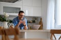 Smiling businessman messaging over smart phone while standing by laptop at kitchen counter at home