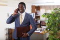 Smiling businessman with portfolio in hands talking on phone in office