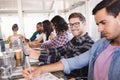 Smiling businessman sitting amidst colleagues working at office Royalty Free Stock Photo