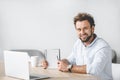 smiling businessman sitting at workplace with laptop and pointing at blank notebook