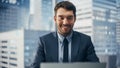 Smiling Businessman in a Suit Sitting at a Desk in Modern Office, Using Laptop Computer, Next to Royalty Free Stock Photo