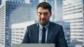 Smiling Businessman in a Suit Sitting at a Desk in Modern Office, Using Laptop Computer, Next to Royalty Free Stock Photo