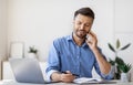 Smiling Businessman Taking Notes While Having Phone Conversation In Office Royalty Free Stock Photo