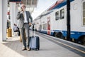 Smiling businessman talking on smart phone while waiting at train station platform