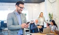 Smiling businessman using phone in the office with colleagues in the background. Royalty Free Stock Photo