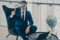 Smiling businessman using VR headset glasses while sitting in office lobby and working on laptop Royalty Free Stock Photo