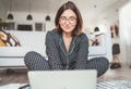 Smiling  Businesswoman dressed pajamas typing notebook keyboard chatting with colleagues sitting cross-legged on living room floor Royalty Free Stock Photo