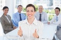 Smiling businesswoman giving thumbs up with her team behind Royalty Free Stock Photo