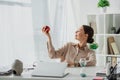 Smiling businesswoman holding apple at workplace with Buddha head, laptop and sand clock in office Royalty Free Stock Photo