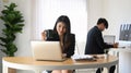 Smiling businesswoman holding coffee cup and working with laptop computer while sitting with her colleague. Royalty Free Stock Photo