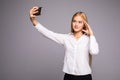 Smiling businesswoman making selfie photo on smartphone. Standing over gray background Royalty Free Stock Photo