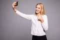 Smiling businesswoman making selfie photo on smartphone. Standing over gray background Royalty Free Stock Photo