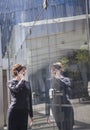 Smiling businesswoman on the phone outside in Beijing looking at her reflection in the glass of the building