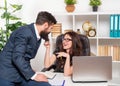 Smiling businesswoman pulling businessman sitting on office desk by beard, flirting