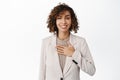 Smiling businesswoman, saleswoman hold hand on chest, express devotion to client, making promise, standing in suit over