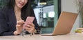 Smiling businesswoman sitting at her office desk front of laptop computer and using smart phone Royalty Free Stock Photo