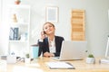 Smiling businesswoman in suit using laptop while talking on mobile phone at desk in home office Royalty Free Stock Photo