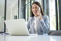 Smiling businesswoman talking on mobile phone and using laptop in office. Royalty Free Stock Photo