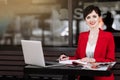 Smiling businesswoman talking working on a laptop and doing notes at cafe on terrace in urban city. Office worker