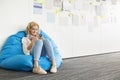 Smiling businesswoman using mobile phone on beanbag chair in creative office