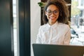 African businesswoman working laptop while standing near window in coworking and looking camera Royalty Free Stock Photo