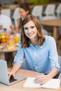 Smiling businesswoman writing on notepad while using laptop in office cafeteria Royalty Free Stock Photo