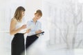 Smiling businesswomen with tablet PC and folder working by railing in office