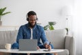 Smiling busy young black businessman freelancer or student with beard in headphones with pc making notes, study