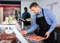 Smiling butcher standing in butcher shop with tray of fresh raw meat steak cutlets Royalty Free Stock Photo