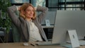 Smiling calm relaxed 40s business woman finished computer work stretching sitting at desk in modern office. Happy middle Royalty Free Stock Photo