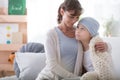 Smiling caregiver supporting sick child with cancer wearing blue headscarf