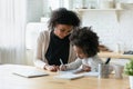 Smiling caring African American mother helping to daughter with homework