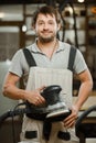 Smiling carpenter stand with eccentric grinding machine in hands Royalty Free Stock Photo