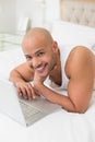 Smiling casual bald man using laptop in bed Royalty Free Stock Photo