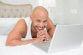 Smiling casual bald man using laptop in bed Royalty Free Stock Photo