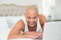 Smiling casual bald young man using laptop in bed Royalty Free Stock Photo