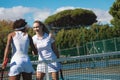 Smiling caucasian female tennis player shaking hands with african american competitor at court