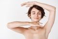 Smiling caucasian girl showing glowing healthy facial skin, standing half naked on white background. Young woman with