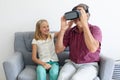 Smiling caucasian granddaughter sitting on couch beside grandfather wearing vr headset
