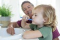 Smiling caucasian grandfather in bathroom kneeling beside grandson brushing teeth