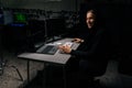 Smiling caucasian hacker man in hood breaking into corporate data servers using laptop and computers sitting at desk in