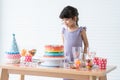 Smiling Caucasian little kid girl in cute dress, surprised on birthday party, looking at beautiful rainbow cake decorated with Royalty Free Stock Photo