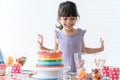 Smiling Caucasian little kid girl in cute dress, surprised and excited on birthday party, looking at beautiful rainbow cake Royalty Free Stock Photo