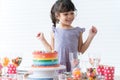 Smiling Caucasian little kid girl in cute dress, surprised and excited on birthday party, looking at beautiful rainbow cake Royalty Free Stock Photo
