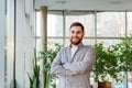 Smiling caucasian man standing near window in office. Successful bearded young smart man with crossed arms. Handsome businessman Royalty Free Stock Photo