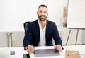 Smiling caucasian mature man with beard in suit sits at table with laptop