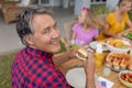 Smiling caucasian senior man holding hamburger with family eating meal together in garden Royalty Free Stock Photo