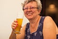 Smiling caucasian senior woman with gray hair holding and drinking glass of light beer in craft czech brewery. Royalty Free Stock Photo