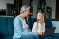 Smiling caucasian small granddaughter and old grandma have video call on computer, study online, play on sofa